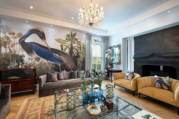 The wallpaper in the luxurious living room features a striking mural of a crane, reflecting the 2021 trends. The design includes intricate details with shades of white and grey for the crane, set against a soft, muted background that may include blues or greens. Elements such as delicate feathers and water motifs add to its elegance.