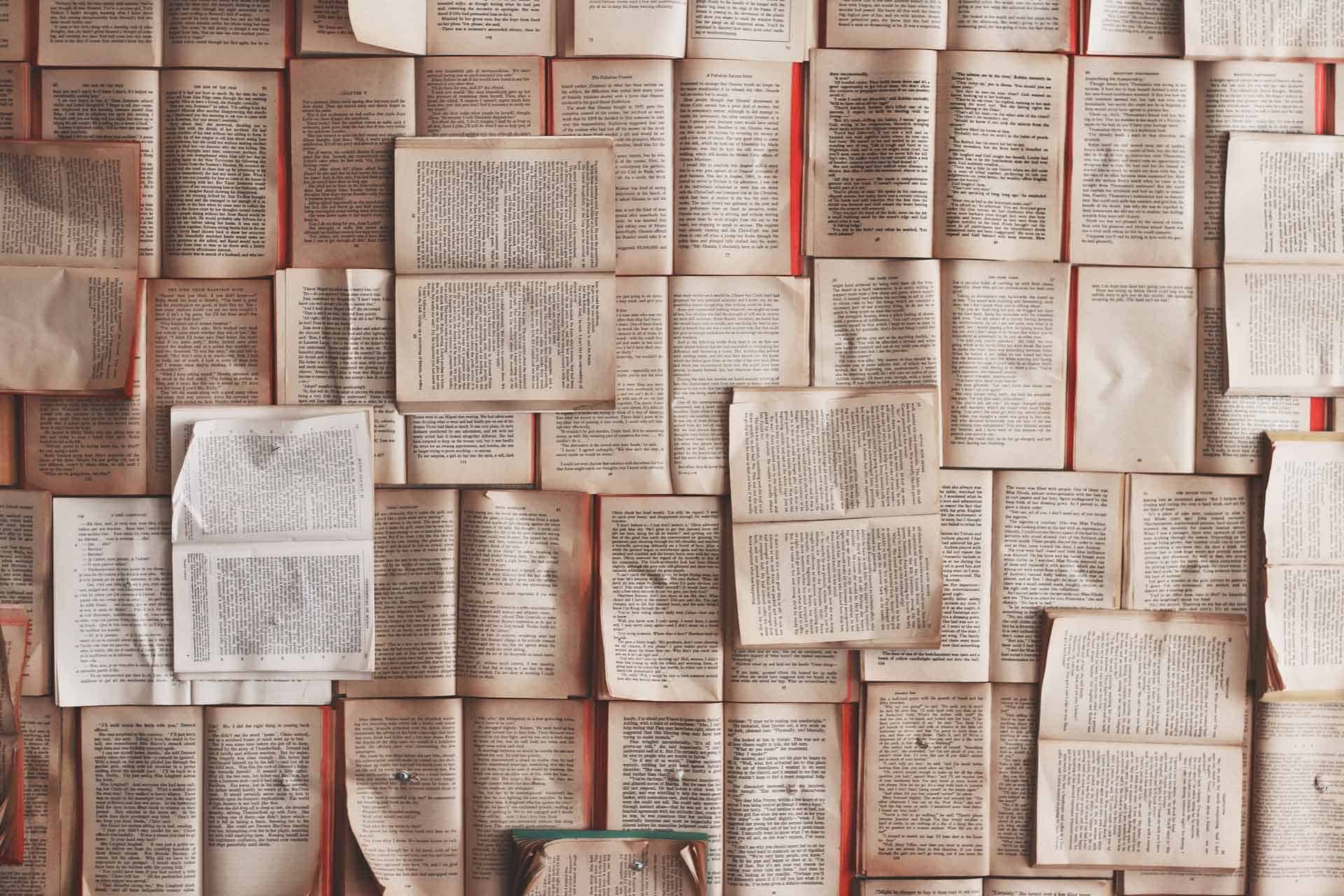 The wallpaper is a dense collage of open books in various sizes and orientations, displaying pages filled with text. The pages show subtle wrinkles and minor tears. The primary colors are off-white to yellowish hues of the paper, with black or dark grey text.