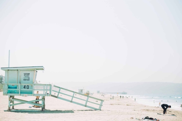 Wallpaper: Sunlit beach with lifeguard tower marked '40' on stilts (left side). Several distant figures enjoying beach and waves. Individual bending near shore break. Clear, hazy sky.
Colors: sky blue, sandy beige, ocean blue-green, white wave crests.