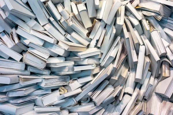 Wallpaper features a large, chaotic pile of books primarily with white covers and pages, arranged in a swirling pattern. Some books are open, others are closed. The scene conveys disarray and abundant knowledge through the dominance of white tones mixed with subtle hints of text and illustrations on pages.