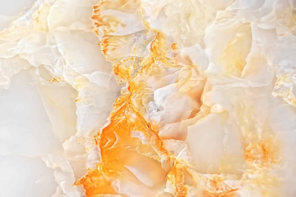 A close-up wallpaper image of polished onyx displays a blend of creamy white, yellow, and amber hues. These colors form abstract, flowing patterns, with the warm amber tones adding visual appeal and organic texture.