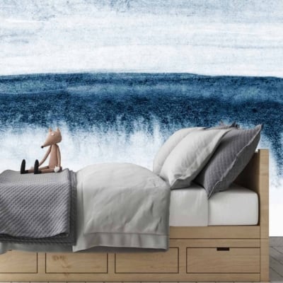 The wallpaper behind the bed is an abstract mural showcasing various shades of blue and white, creating a design reminiscent of the sea. The elements include wave-like patterns and fluid shapes, evoking a sense of movement and tranquility. Predominantly featuring hues of navy, sky blue, turquoise, and crisp white accents, the mural adds a serene backdrop to the bedroom's minimalist design.