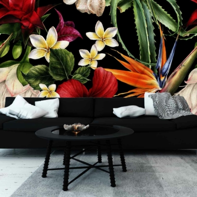 A modern living room boasts a vibrant, bold floral mural with tropical flowers and greenery. The wallpaper features an array of colors including vivid reds, lush greens, and bright yellows against a dark backdrop. This eye-catching design creates a striking focal point in the space.