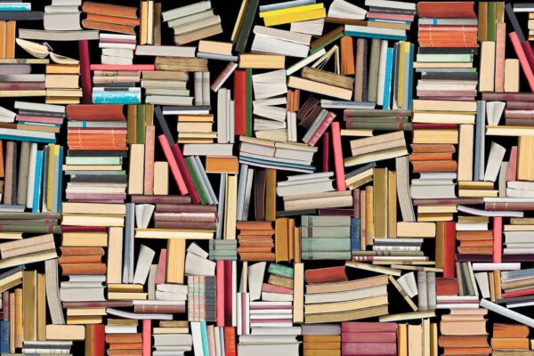 Discover a vibrant, disordered collage of books on the wallpaper. The scene features books of diverse sizes and hues—rich reds, serene blues, vivid yellows, deep greens, and soft pastels. These books are stacked and scattered every which way: horizontally, vertically, and diagonally. The jumbled arrangement showcases an overwhelming yet intriguing abundance of knowledge in every corner.