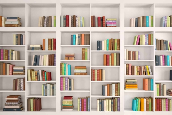 The wallpaper features a wall of white bookshelves filled with various books of different sizes and colors. The organized display has books placed vertically and stacked horizontally, creating a colorful and visually appealing library setting.