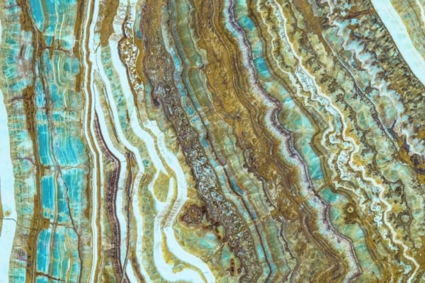 A polished Marmala stone surface exhibits intricate, layered patterns with vibrant shades of turquoise, brown, and white. Wavy, organic lines weave through the texture, creating an abstract appearance. The colors blend seamlessly to form a visually striking and complex design perfect for a wallpaper.