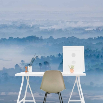 Expansive misty blue forest wallpaper featuring varying shades of blue and teal. Tree silhouettes create depth, with hazy gradients transitioning from dark to light blues. Subtle hints of green interspersed among the foliage offer a touch of tranquility, emphasizing the serene ambiance. The overall mood is calm and peaceful, ideal for a minimalist workspace background.