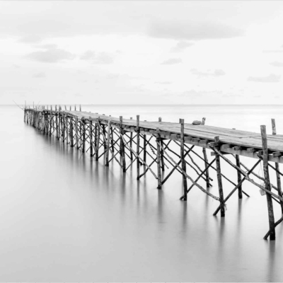 Wallpaper: A black and white image of a long wooden pier extending into calm water, overcast sky, serene atmosphere, tranquil setting. Reflection of the pier in still water.