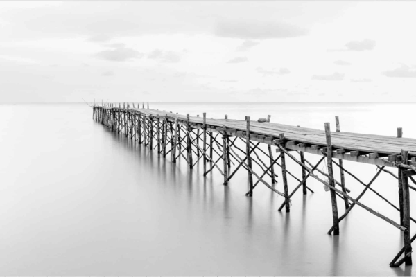 Wallpaper: A black and white image of a long wooden pier extending into calm water, overcast sky, serene atmosphere, tranquil setting. Reflection of the pier in still water.