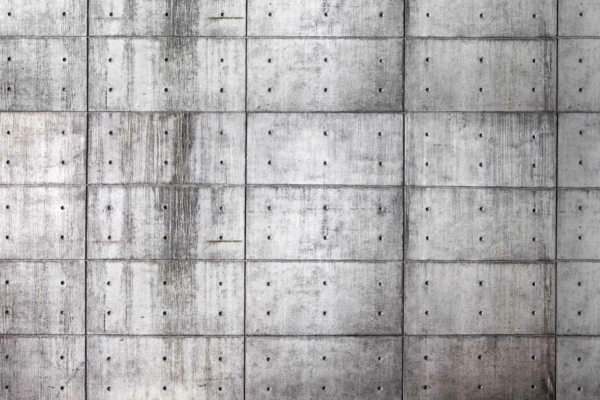 The wallpaper shows a close-up of a large concrete wall with a raw, grid pattern. It features rectangular concrete slabs, each marked by small circular indentations arranged regularly. There are faint vertical streaks on some slabs indicating slight weathering. The colors are predominantly shades of gray, ranging from light to dark tones. Key elements: concrete texture, grid pattern, circular indentations, weathered streaks, gray hues.