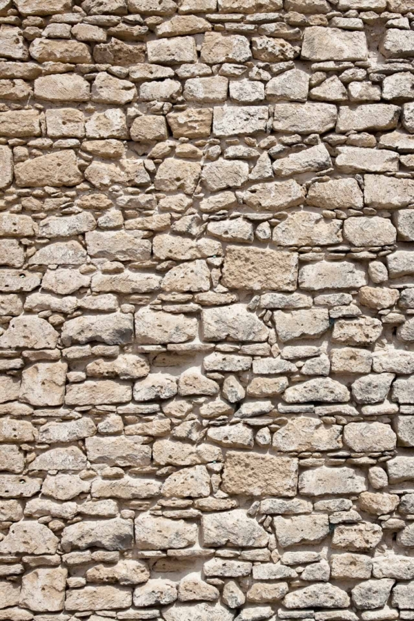 A wallpaper featuring a textured wall made of irregularly shaped light beige stones, unevenly stacked and fitted together. Minimal visible mortar between the stones enhances the rustic beauty reminiscent of Rhodes, Greece. The stones vary in size and shape, creating a rough and charming appearance with natural earthy tones.