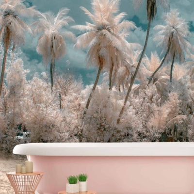 Surreal landscape wallpaper featuring a pastel pink bathtub, tall light pink palm trees, a cloudy teal-colored sky, subtropical elements with small matching tables, candles, and plants for a whimsical and dreamy outdoor bathroom setting.