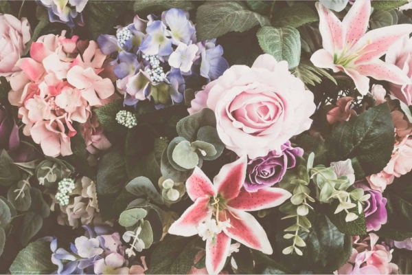Wallpaper featuring a vibrant assortment of pink roses, lilies, hydrangeas, and lilacs, all surrounded by lush green leaves. This spring-inspired design is densely packed with colorful blooms. Key elements: flowers, rosy pinks, whites from lilies, pastel blues of hydrangeas, purples from lilacs, lush greenery. Rich and colorful floral fever for the senses.
