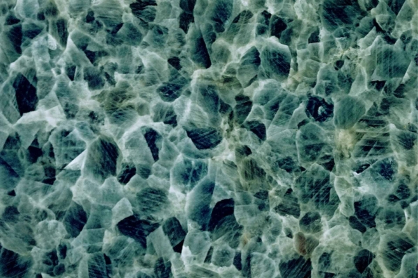 Close-up image of intricate mineral or crystal surface wallpaper. Features a mosaic of interlocking, angular shapes in shades of blue, green, and grey. Rough, layered texture with light reflecting off different facets. Highlight: Mineral texture, crystal patterns, blue hues, green tones, grey shades.