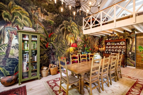 The wall mural features lush green palm leaves, vibrant tropical flowers in hues of red, yellow, and pink, and playful toucans. This tropical-themed wallpaper brings a lively burst of nature-inspired colors and exotic patterns to the dining room.