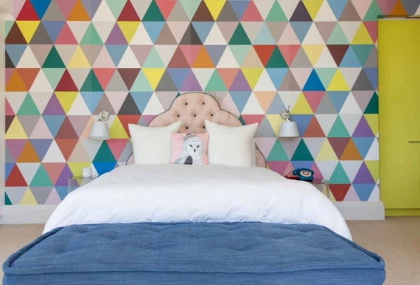 The wall showcases a vibrant geometric pattern with multicolored triangles. The design features bold colors like red, blue, yellow, green, and purple. Each triangle is sharply defined, creating an eye-catching mosaic that adds a dynamic element to the room. This colorful wallpaper serves as a lively backdrop that can enhance any home decor portfolio by introducing energy and visual interest into the space.