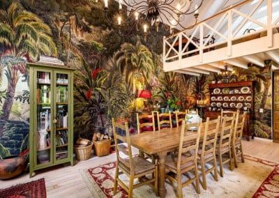 Tropical jungle mural wallpaper featuring lush green foliage, vibrant flowers in reds, pinks, and oranges, exotic birds in blues and yellows, playful monkeys swinging on vines, and rich brown tree trunks woven throughout.