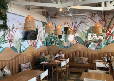 The wallpaper features vibrant tropical murals with lush greenery, including large palm leaves and colorful birds. The dominant colors are shades of green, bright blues, yellows, and splashes of red. There are also tropical flowers in pinks and oranges interspersed throughout the design.