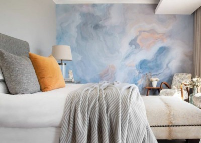 A striking blue and pink abstract wall mural graces the modern bedroom, featuring elements of swirling patterns and bold hues. The vivid blend of blue and pink creates a captivating focal point, enhancing the serene ambiance.