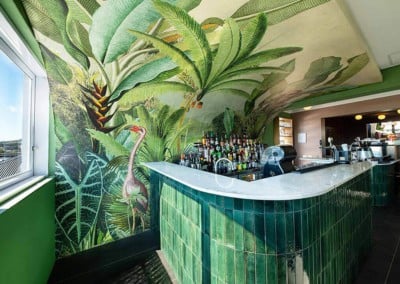 Wallpaper boasts lush green plants, tropical leaves, vibrant ferns, and exotic flowers. Predominantly green with touches of bright accents and intricate foliage patterns. Pops of color in floral elements.