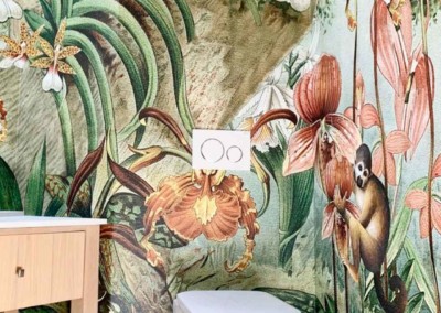 The wallpaper features vibrant jungle-themed elements, including exotic flowers, lush green plants, and playful monkeys. The colors are bright and lively, with a palette that includes bold greens, striking reds, sunny yellows, and rich purples. These elements create an eye-catching and dynamic backdrop perfect for a modern bathroom setting.