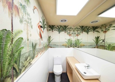The wallpaper features vibrant murals of flamingos, palm trees, and lush green plants. The colors include vivid pinks (flamingos), rich greens (palm trees and plants), sandy tans, and tropical blues.