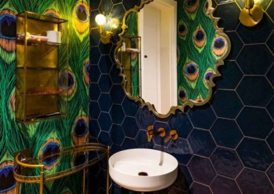 The bathroom boasts a striking accent wall featuring peacock feather patterned wallpaper. The design showcases vibrant teal, turquoise, and gold hues with intricate feather details.