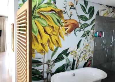 Tropical botanical-themed wall mural with lush green palm leaves, vibrant monstera plants, colorful hibiscus flowers in shades of pink and red, and exotic birds like toucans and parrots. Rich greens, lively pinks, deep reds, and accents of yellow dominate the design.