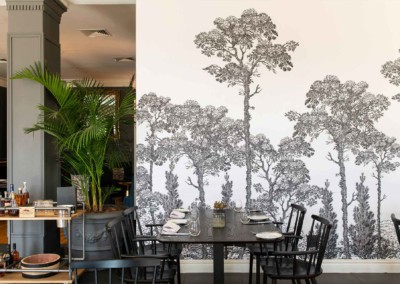 Modern dining area featuring a monochrome forest mural. The wallpaper showcases intricate details of trees and foliage in shades of black, white, and grey. The elegant design adds depth and a contemporary touch to the space, making it a striking focal point for any interior setting.