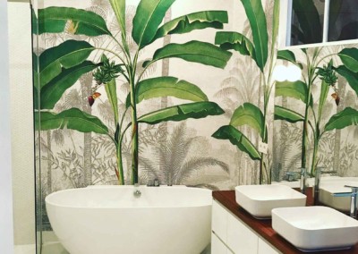The bathroom features tropical-themed wallpaper behind the white bathtub, showcasing large green banana leaves. The wallpaper elements include lush greenery with varying shades of verdant green, creating a natural, vibrant backdrop. Perfect for enhancing your home's portfolio with its fresh and exotic ambiance.
