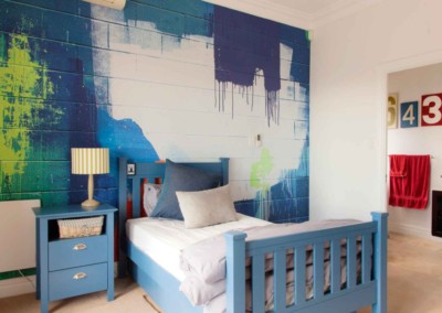 The wallpaper in the bedroom features a dynamic blue and green abstract mural. The design is bold with rich hues of blue and vibrant shades of green, blending seamlessly to create an artistic backdrop. This visually striking pattern sets a lively tone for the room.
