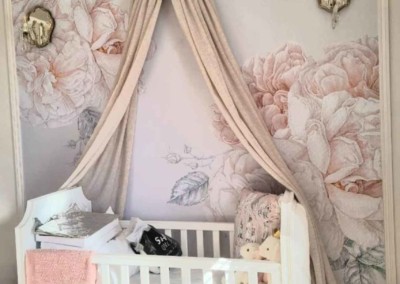 The wallpaper features large pastel floral prints in shades of soft pink, lavender, and mint green. Delicate petals and lush leaves create an elegant, serene backdrop perfect for a cozy nursery setting.