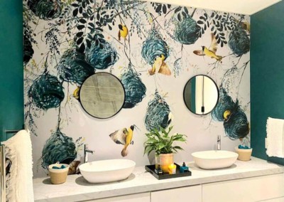 A vibrant mural features birds, nests, and teal elements between two round mirrors.
