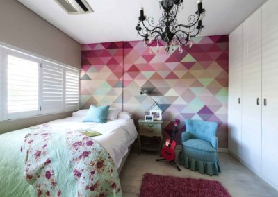 The wall displays a colorful geometric mural featuring bold patterns and vibrant hues, including shades of blue, red, yellow, and green. The shapes are intricately arranged in a modern, eye-catching design that adds artistic flair to the room.