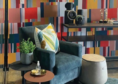 A vibrant, multicolored geometric wall features bold shapes and patterns in shades of red, blue, yellow, green, and purple. Triangles, squares, and hexagons interlock to create an eye-catching mosaic. Perfect for a modern living room setting.