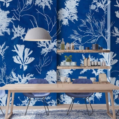 The dining area features a bold blue and white botanical print wallpaper, reminiscent of cyanotype photographic printing. The wallpaper highlights detailed plant motifs in rich blue tones against a stark white background, creating a striking and modern graphic effect. The intricate patterns evoke natural elements, playing with various shades of blue to add depth and interest to the walls.