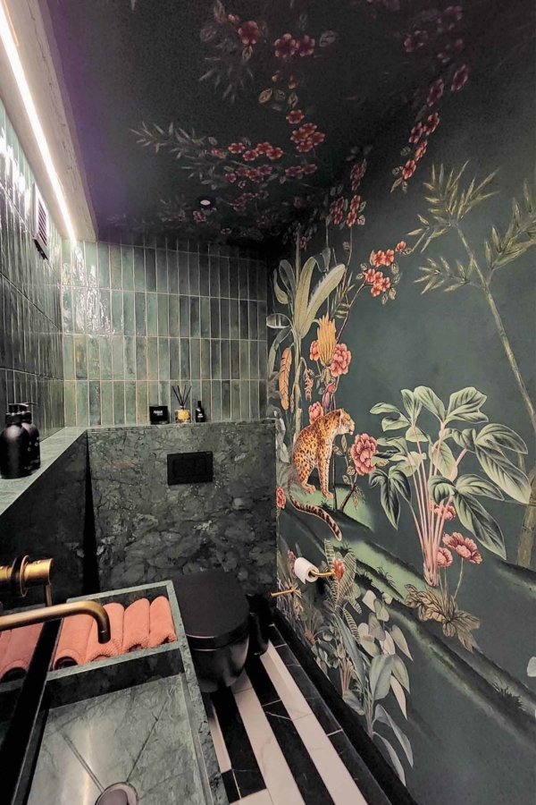 The wallpaper features intricate tropical floral and animal designs with green mosaic tiles as a backdrop. It includes elements like vibrant flowers, lush leaves, and detailed animal illustrations in a rich color palette of greens, pinks, and other natural hues.