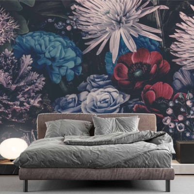 The wallpaper features a large mural of colorful flowers, showcasing vibrant hues such as pink, yellow, blue, and orange. Delicate green leaves and stems add contrast and depth to the design. The floral pattern spreads across the wall behind the bed in a striking yet harmonious arrangement.