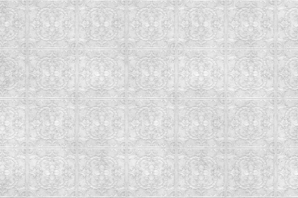 White wall, intricate, raised floral pattern, uniform grid-like repetition, textured appearance, elegant design. Key elements: floral motifs, raised texture. Predominant color: white.