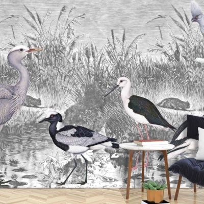 A sophisticated mural showcases wading birds such as herons and cranes amidst a serene wetland scene. The design features a monochromatic palette, emphasizing shades of gray, black, and white to depict the natural elements like water, reeds, and distant trees. This wallpaper combines elegance with a nature-inspired aesthetic.