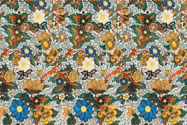 A vibrant and intricate floral wallpaper pattern featuring blue, yellow, orange, and white blossoms interwoven with green foliage. Detailed ornamental designs against a light, textured background highlight Sadie's sophisticated touch. Key elements: colorful flowers, green foliage, detailed designs, light background.