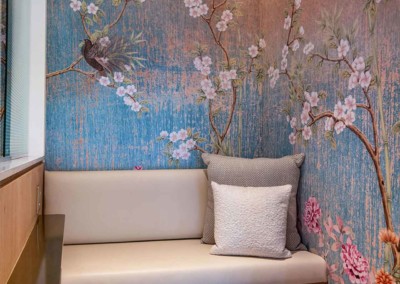Brightly colored wall mural featuring birds, branches, and flowers. Elements include intricately illustrated birds perched on delicate branches intertwined with vibrant blossoms. Colors dominate with hues of green from the foliage, brilliant bluebirds, vivid pink and red flowers, and subtle touches of yellow and orange detailing. Perfect for creating a nature-inspired focal point in home décor designs!