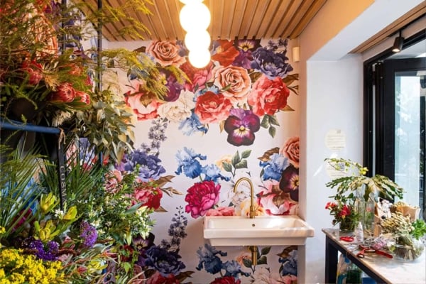 The wallpaper features a vibrant design with large, colorful flower prints in shades of red, pink, blue, yellow, and green. The floral patterns are intricate and lush, making the room feel lively and fresh.