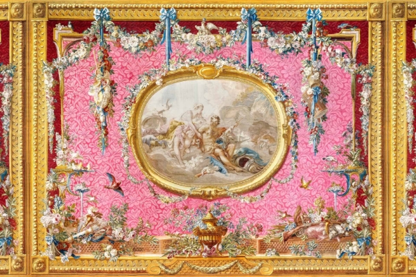 The wallpaper features a vivid pink, tapestry-like background adorned with intricate floral designs and ornamental frames. The designs include detailed flower patterns such as daisy chains intertwined with other decorative elements. The colors are predominantly shades of pink, with accents of green (for leaves and stems), white (highlighting the daisies), gold and silver (in the frames and ornate details).