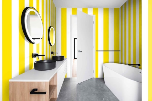 This modern bathroom showcases "The Right Stripe" wallpaper, featuring bold vertical stripes in yellow and white.