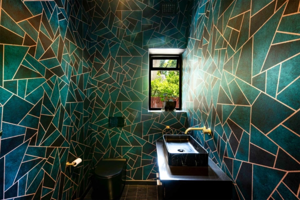 A modern bathroom features teal and gold geometric tile wallpaper. The wallpaper incorporates striking teal hues with contrasting gold accents in a geometric pattern.