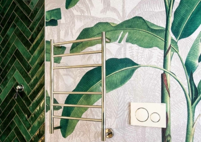 The bathroom features a tropical-themed wallpaper with large green leaves. The lush foliage patterns are vibrant, featuring shades of emerald and lime green, adding to the tropical ambiance.