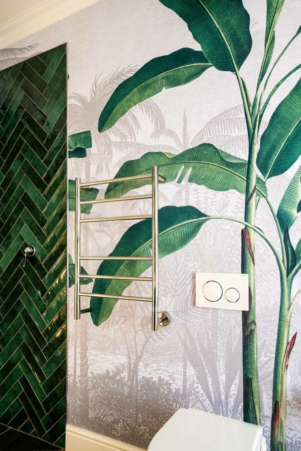 The bathroom features a tropical-themed wallpaper with large green leaves. The lush foliage patterns are vibrant, featuring shades of emerald and lime green, adding to the tropical ambiance.