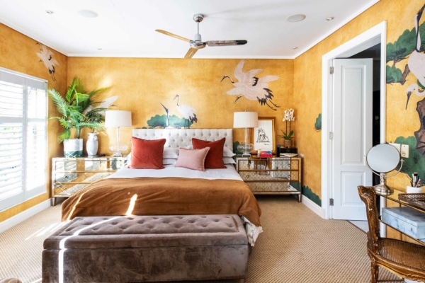 The wallpaper features warm, golden-yellow tones with elegant crane murals. The cranes are depicted gracefully, adding a touch of nature and sophistication. The mural highlights delicate details in shades of white and light gray, contrasting beautifully against the rich yellow backdrop.