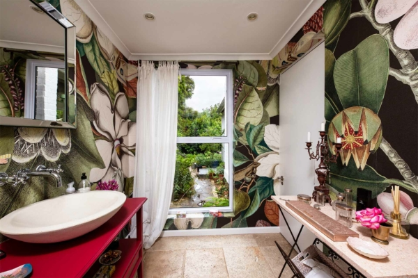 Our vibrant bathroom features a stunning large botanical wallpaper, showcasing lush green leaves, vivid tropical flowers in shades of pink, red, and orange, and intricate vines. This striking design sets a lively backdrop with its rich array of natural elements and vibrant colors.